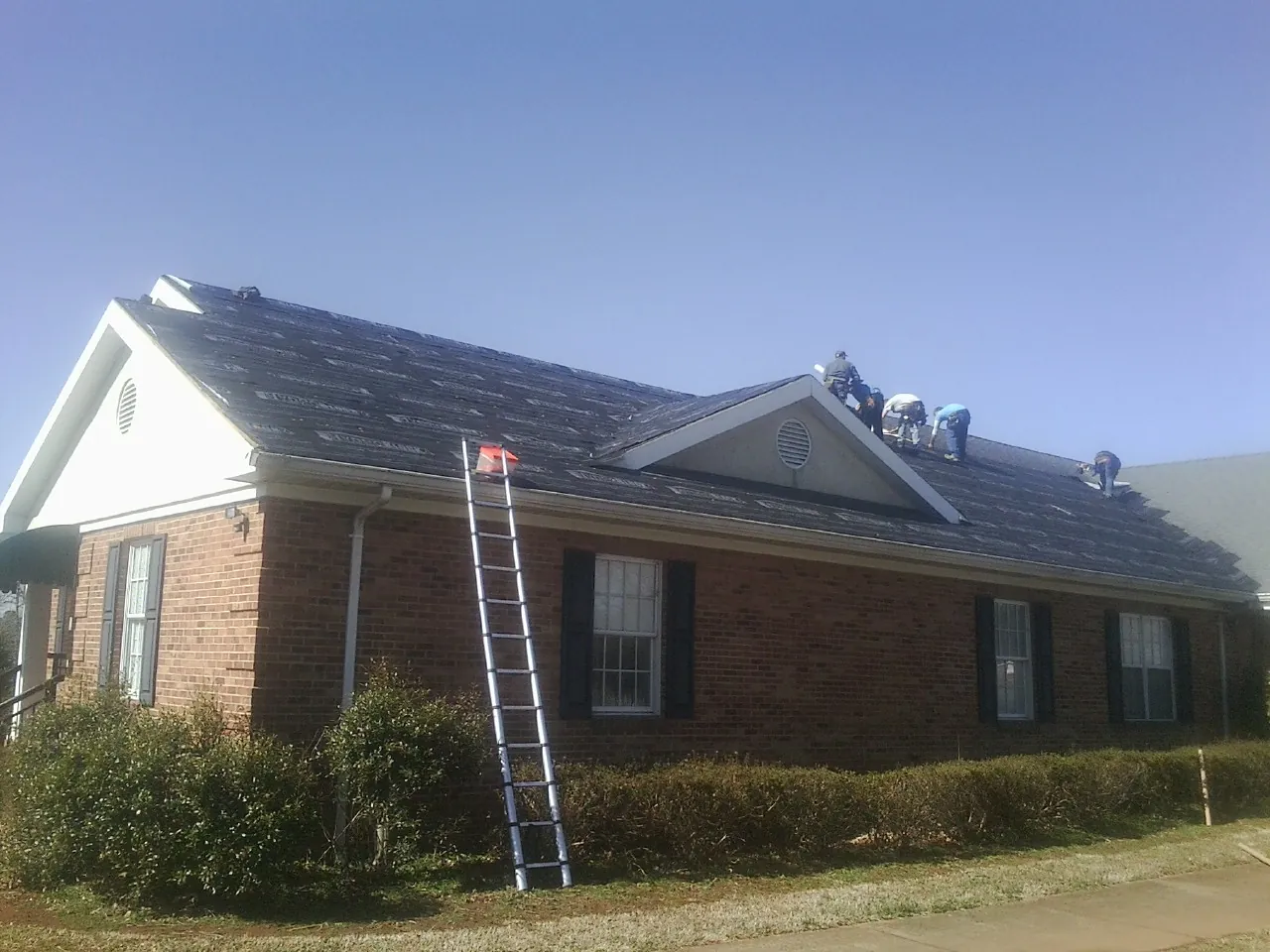Crew tearing shingles off a brick ranch roof with a ladder set — Emergency Roof Repair work by our crew in Mahnomen