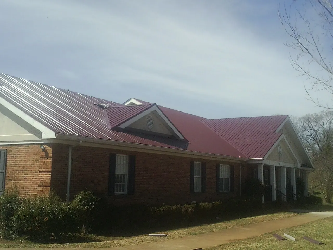 Red metal roof with gabled entries on a long brick building, from a Hail Damage Roof Repair job in Mahnomen