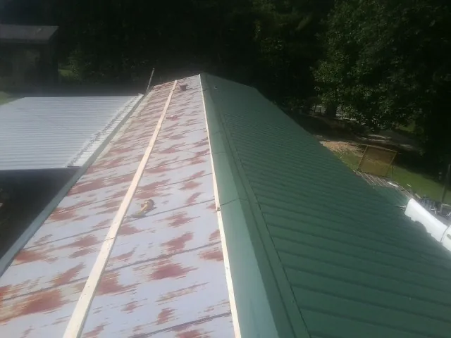 Old rusted panels beside newly installed green metal roofing — Wind Damage Roof Repair by Roofing Brothers in Mahnomen