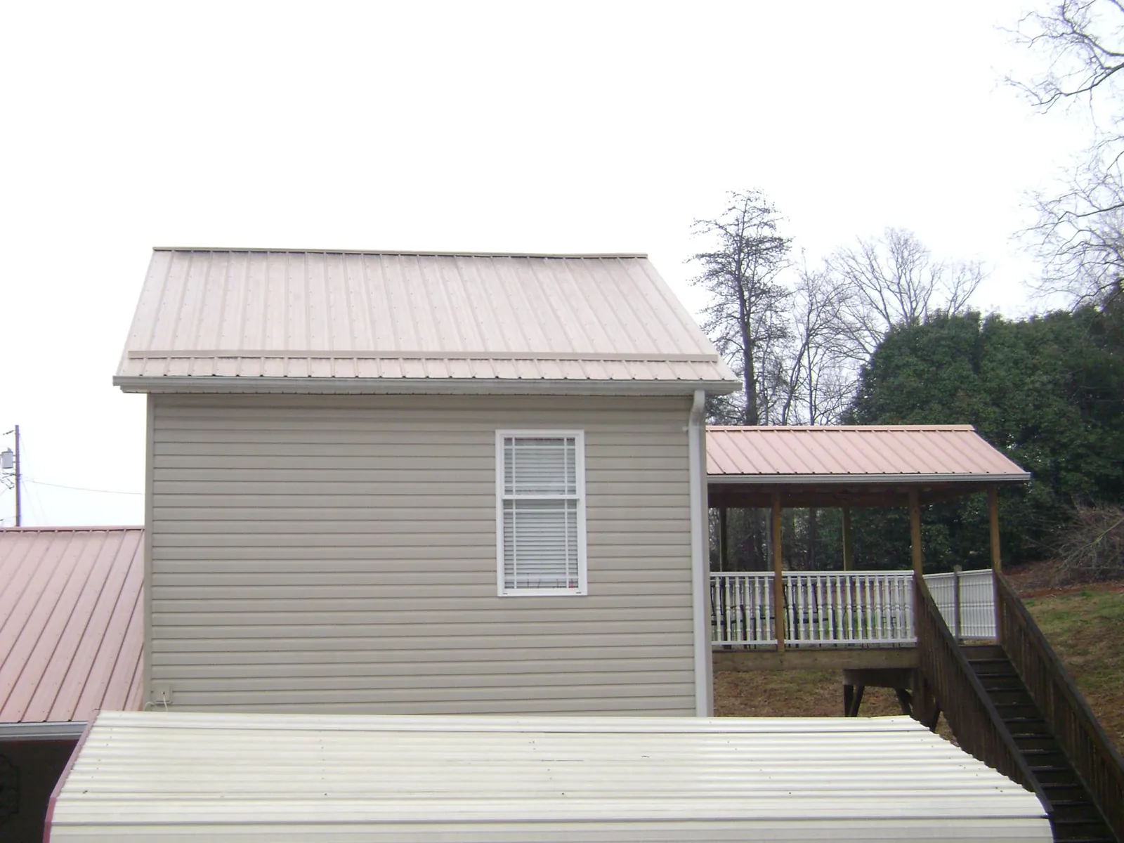 Tan metal roofs on a two story addition and attached porch, from a Roof Replacement job in Mahnomen